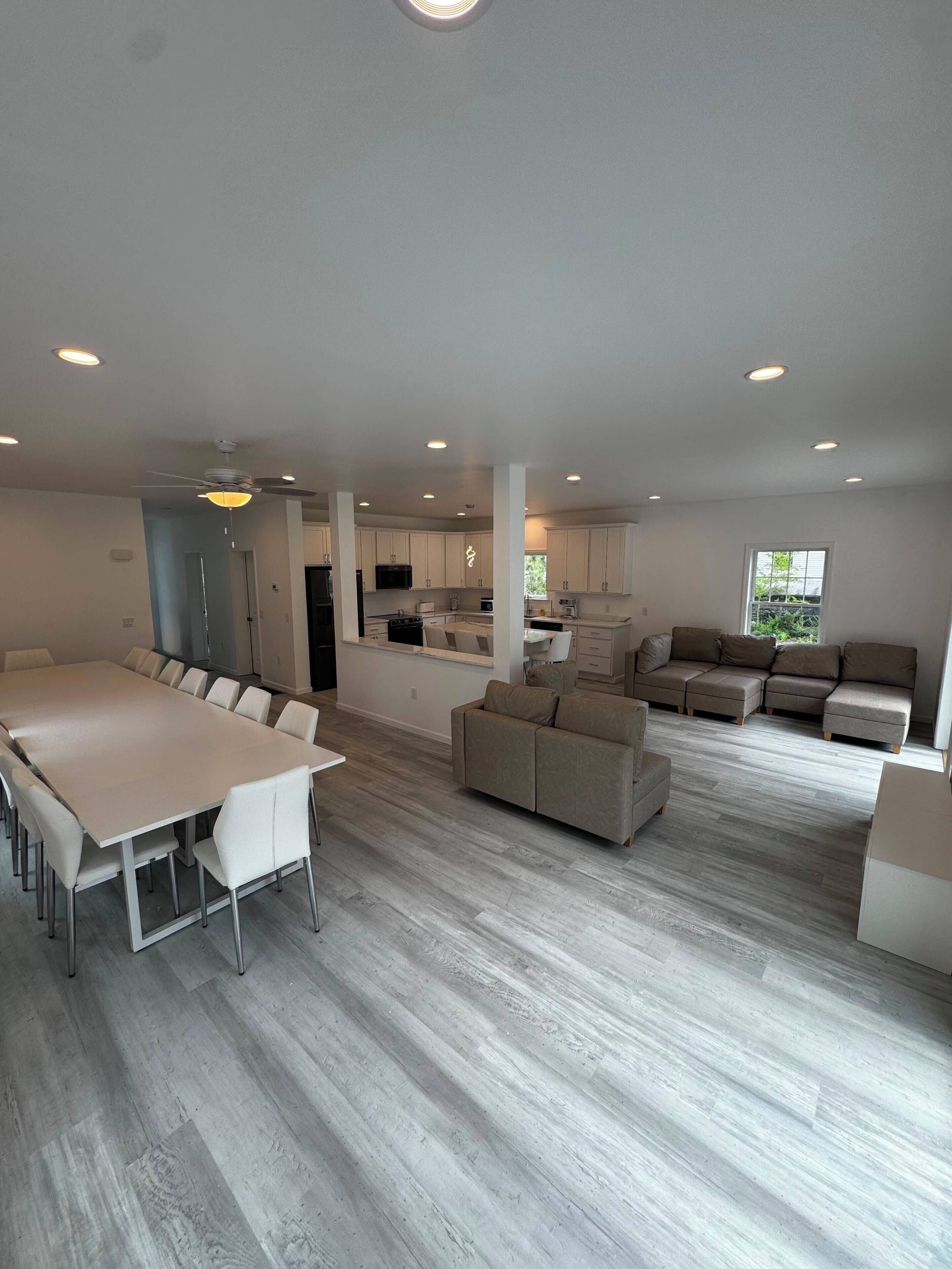 A spacious living area with a large dining table, sofas, and a kitchen in the background.