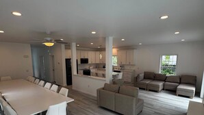 A spacious living area with a large dining table, sofas, and a kitchen in the background.