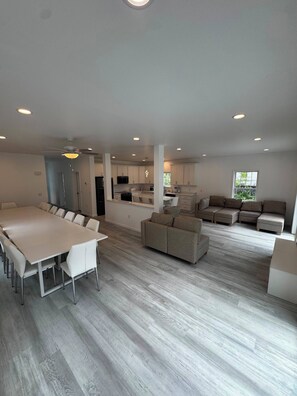 A spacious living area with a large dining table, sofas, and a kitchen in the background.