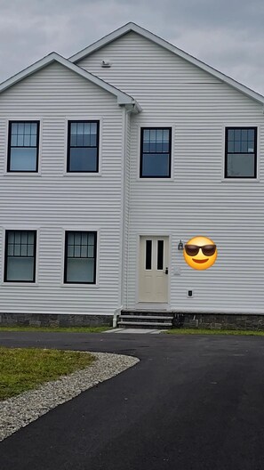 Ein zweistöckiges Gebäude mit einer symmetrischen Fassade, einem zentralen Eingang mit einer Tür und einer kleinen Veranda mit Stufen, die zur Tür hinaufführen.