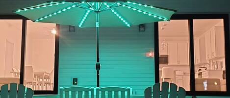 Un espace extérieur aménagé en terrasse, avec une table et des chaises, situé sous une tonnelle décorée de guirlandes lumineuses.