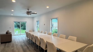 A spacious room with a long table and chairs, a ceiling fan, and large windows.