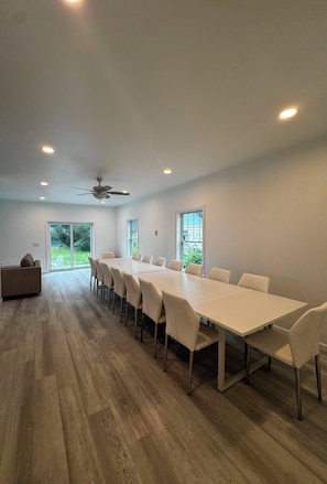 A spacious room with a long table and chairs, a ceiling fan, and large windows.