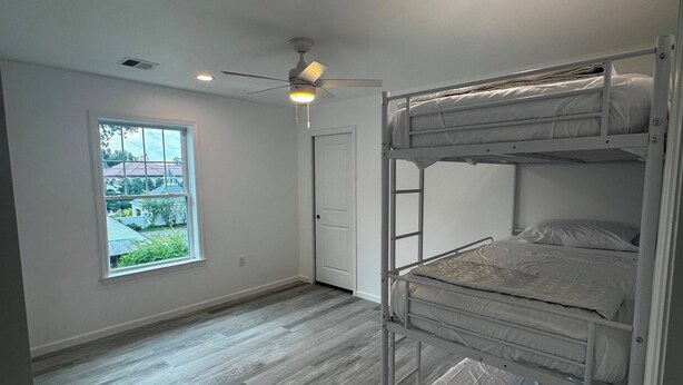 A room with a bunk bed, a ceiling fan, a window with a view, and a door. - Spacious 4-bedroom lake house in Shrewsbury MA.   (Shrewsbury)