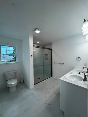 A bathroom with a toilet, a glass-enclosed shower, and a marble sink.