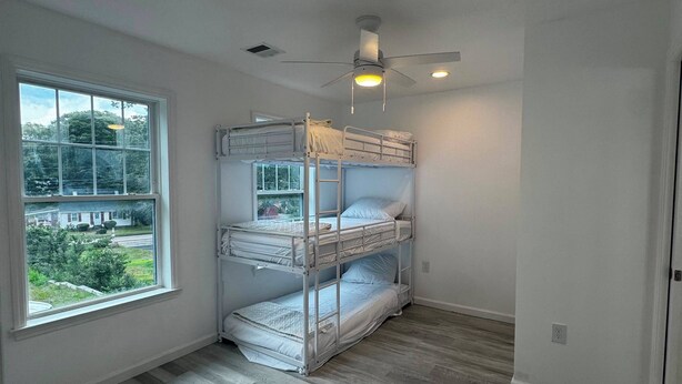 A room with bunk beds, a ceiling fan, and a large window.