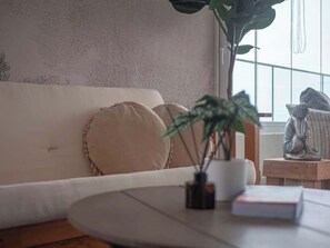 Ein Zimmer mit einem weißen Sofa, einem runden Tisch mit einer Pflanze und einer Statue auf einem Beistelltisch.