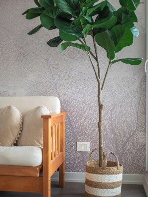Ein Zimmer mit einem hölzernen Bett, einem beigefarbenen Sofa, einer strukturierten Wand und einer Pflanze in einem gestreiften Korb.
