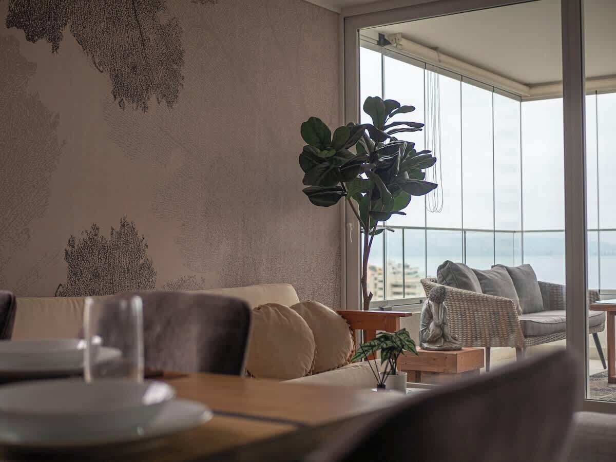 A modern living room with a sofa, a dining table, and a large window offering a view of the cityscape.