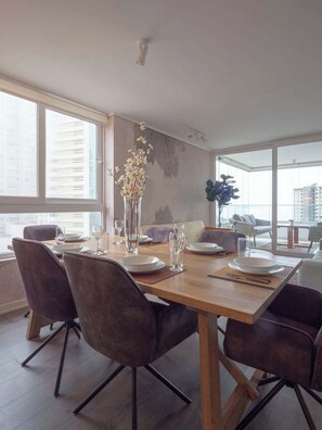A modern dining area with a wooden table, four chairs, and a vase of flowers. - Costa Home - 7 PAX  & Sunset Arena & Vistas al Mar (Concón)