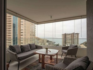 Een balkon met een bank, stoelen en een tafel, met uitzicht op een stadsbeeld en de zee.
