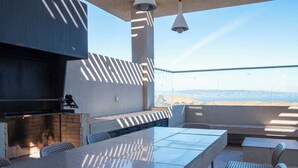 Un patio al aire libre con una mesa larga y sillas, una parrilla y vistas del paisaje.