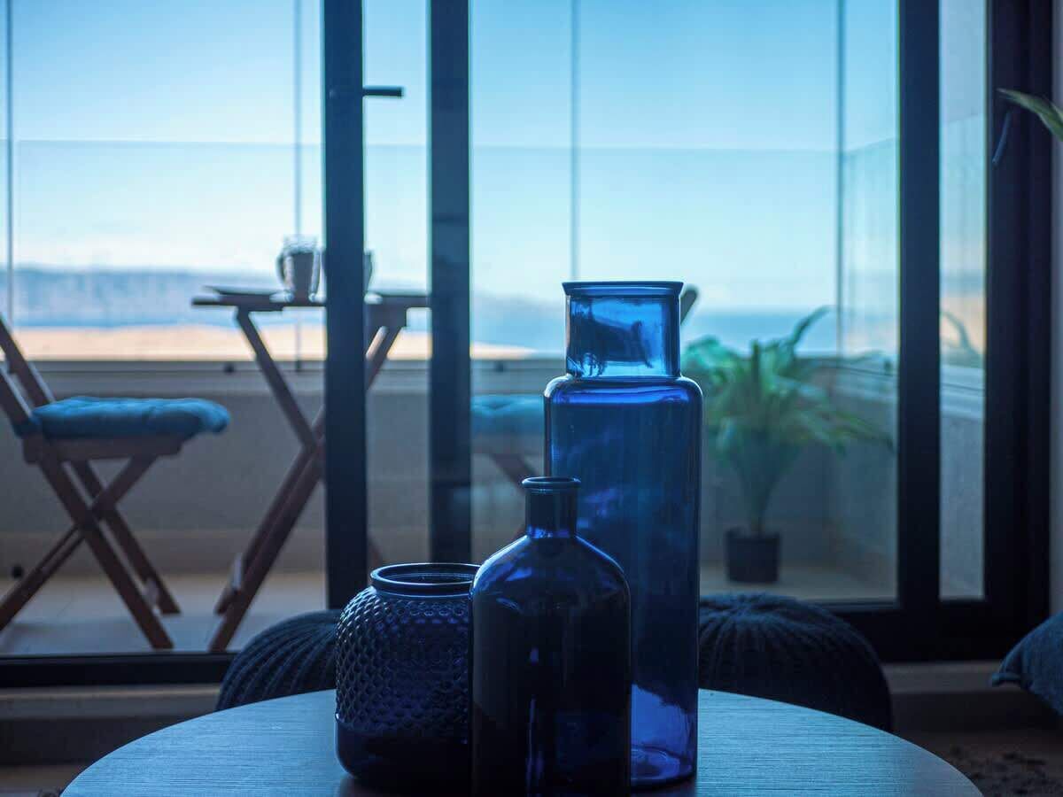 Une pièce avec une grande fenêtre, une table ornée de bouteilles en verre décoratives et une chaise.