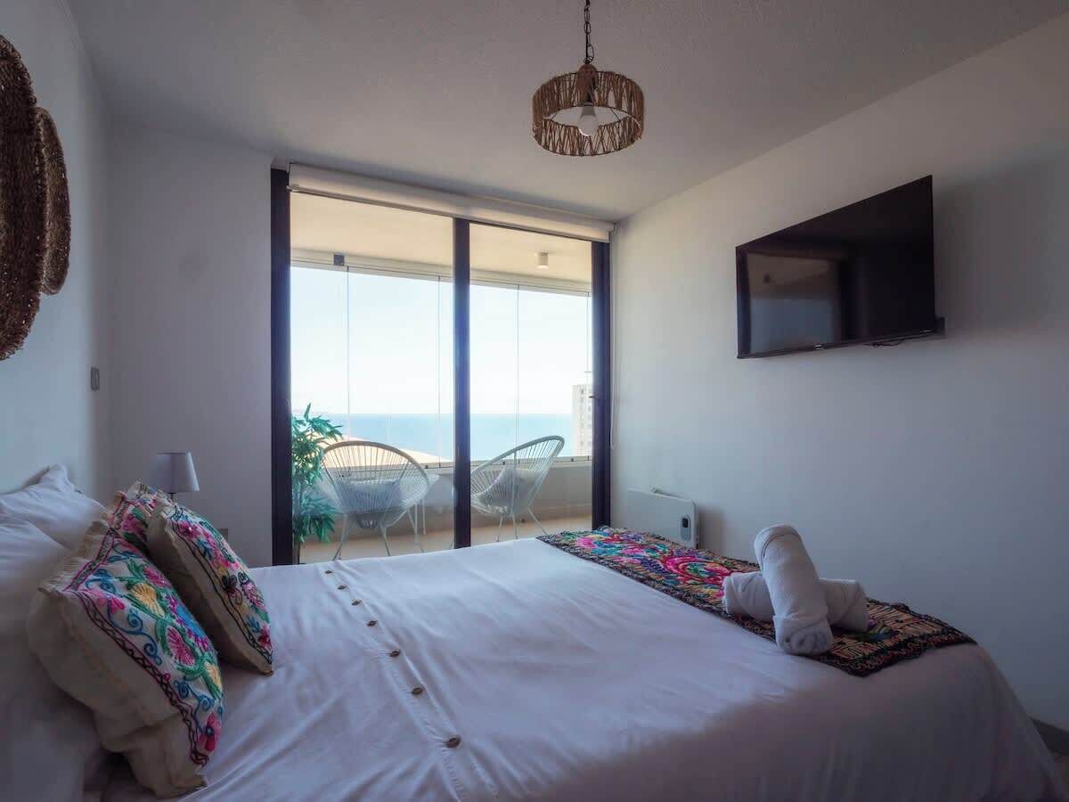 A bedroom with a bed, a TV, and a balcony with chairs.