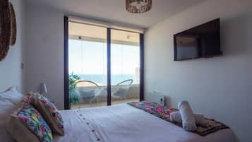 A bedroom with a bed, a TV, and a balcony with chairs.