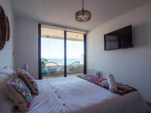 A bedroom with a bed, a TV, and a balcony with chairs. - Costa Home - Departamento Vista Valparaíso (Concón)