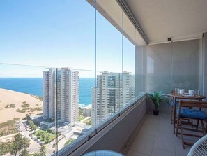 A balcony with a view of the beach and ocean, a small table with chairs, and a potted plant. - Costa Home - Departamento Vista Valparaíso (Concón)