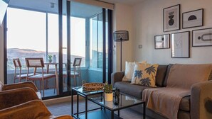 En moderne stue med sofa, sofabord og stole, samt en balkon med bord og stole, og billedkunst på væggene.