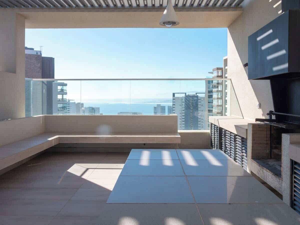 Un balcón moderno con vistas al mar, zona de estar y una parrilla empotrada.