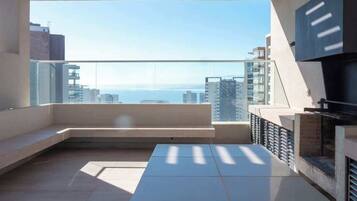 Un balcón moderno con vistas al mar, zona de estar y una parrilla empotrada.