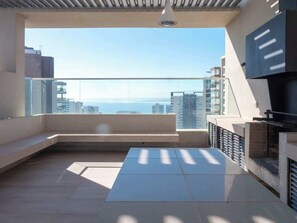 Ein moderner Balkon mit Meerblick, einer Sitzgelegenheit und einem fest installierten Grill.