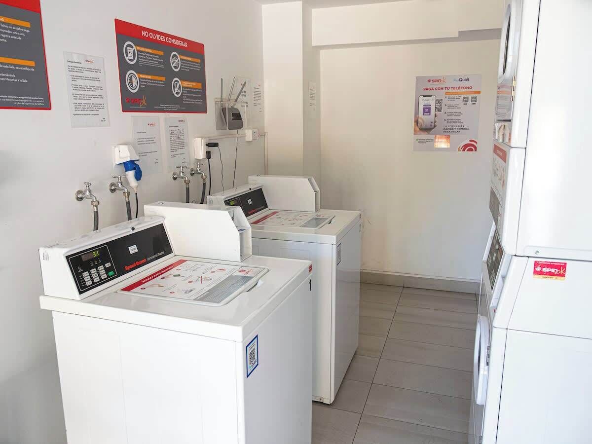 Een wasserette met twee wasmachines en een droogmachine, voorzien van bedieningspanelen en veiligheidsinstructies.
