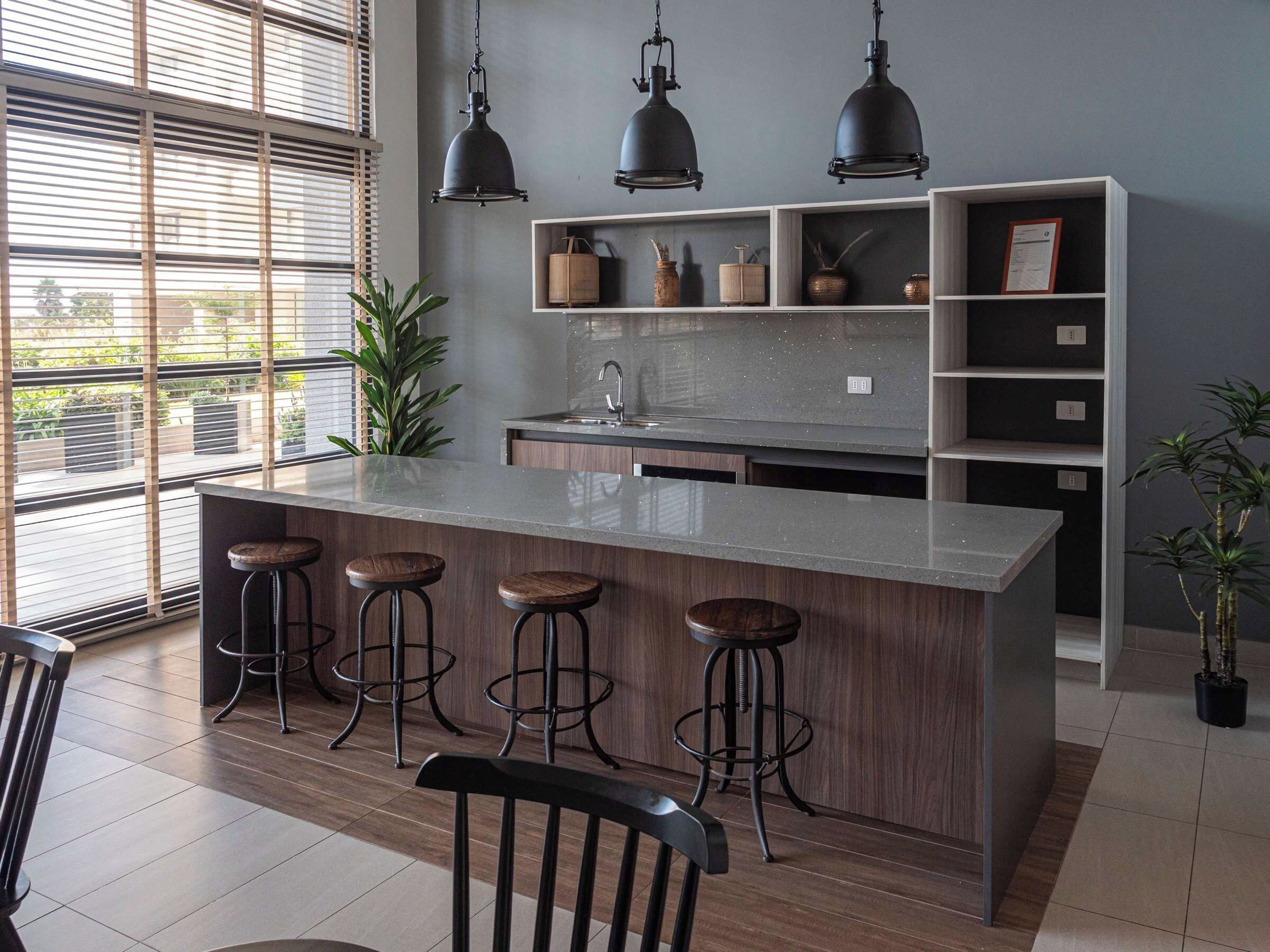 A modern kitchen with a central island, bar stools, pendant lighting, and built-in shelves.