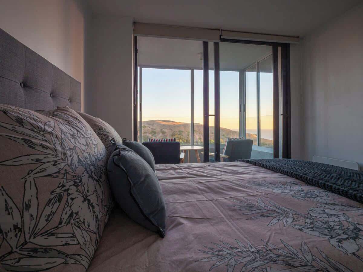 Ein Schlafzimmer mit einem Bett, einem Sessel, einem kleinen Tisch und Blick ins Freie.