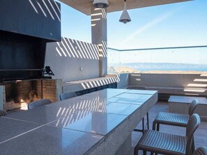 Un área de cocina exterior con una encimera larga, asientos y vistas al paisaje.
