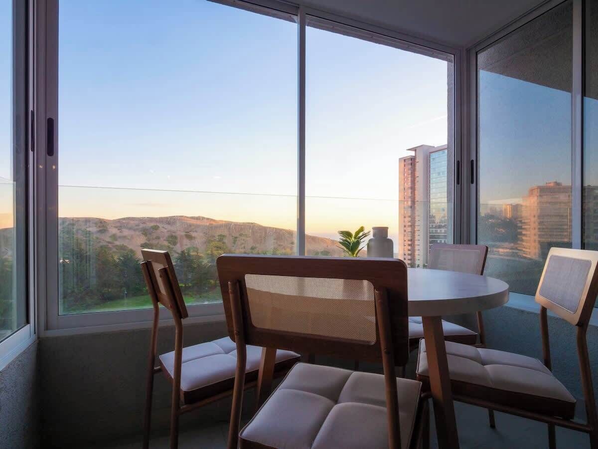 Een balkon met een ronde tafel en stoelen, met uitzicht op een stadsbeeld en heuvels.