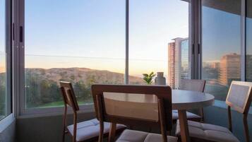 Een balkon met een ronde tafel en stoelen, met uitzicht op een stadsbeeld en heuvels.