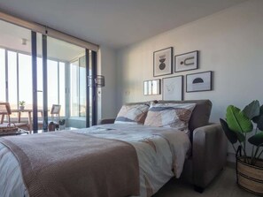 Un dormitorio con cama, una silla, una mesa y un ventanal amplio.