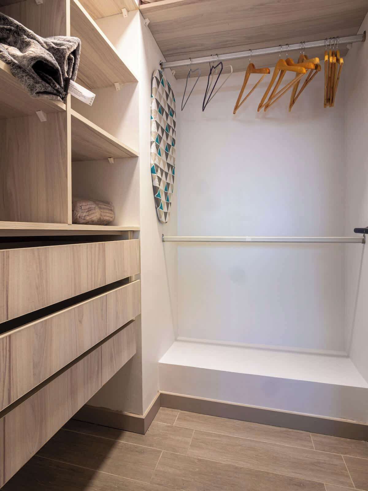 Un dressing avec des étagères en bois, une tringle à vêtements avec des cintres en bois et un porte-serviettes à motifs.