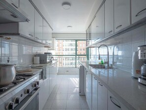 A modern kitchen with white cabinets, a stove, a microwave, and a coffee maker. - Oceanfront Luxury Apt w/ 8 PAX , Pool & Gym (Viña del Mar)