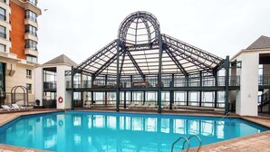 Una piscina interior amb estructura de sostre de vidre, envoltada de gandules i un paviment de rajoles.