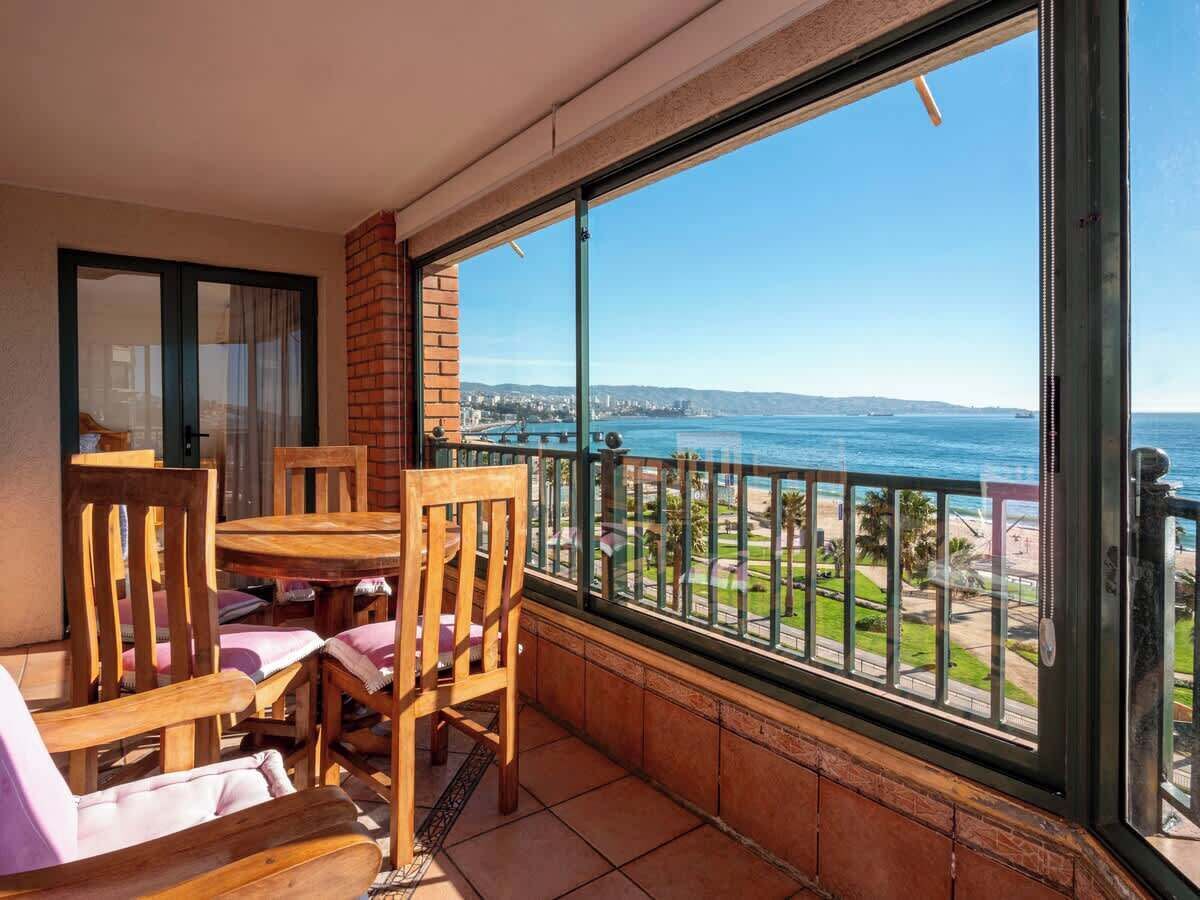 A balcony with a table and chairs, a view of the sea, and a distant cityscape.
