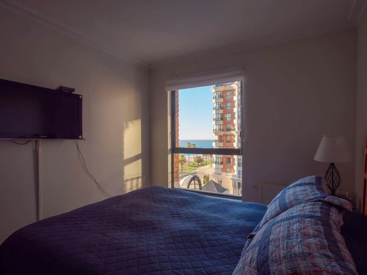 A bedroom with a bed, a television, a window with a view of buildings and a balcony.