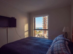 Una camera da letto con un letto, una televisione, una finestra che offre vista su edifici e un balcone.