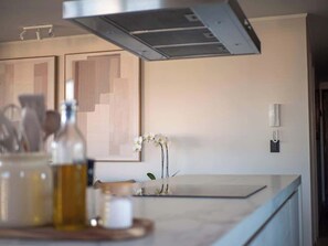 A modern kitchen with a marble countertop, a stainless steel range hood, and a vase with white flowers. - Costa Home 7 PAX - Lujoso - WIFI 1000 MBPS HS (Concón)