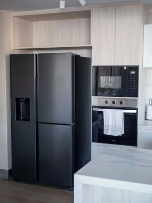 A modern kitchen with a stainless steel refrigerator, a microwave, and an oven. - Costa Home 7 PAX - Lujoso - WIFI 1000 MBPS HS (Concón)