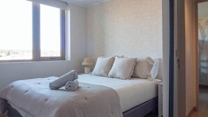 A bedroom with a bed, a bedside table, a lamp, a window, and a door. - Costa Home 7 PAX - Lujoso - WIFI 1000 MBPS HS (Concón)