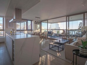 Un intérieur moderne comprenant une cuisine, un coin repas et un espace salon avec de grandes fenêtres.
