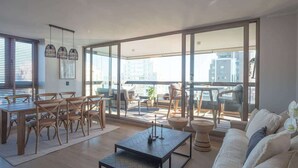 A spacious living area with a dining set, a sofa, and a balcony with a view of the city. - Costa Home 7 PAX - Lujoso - WIFI 1000 MBPS HS (Concón)