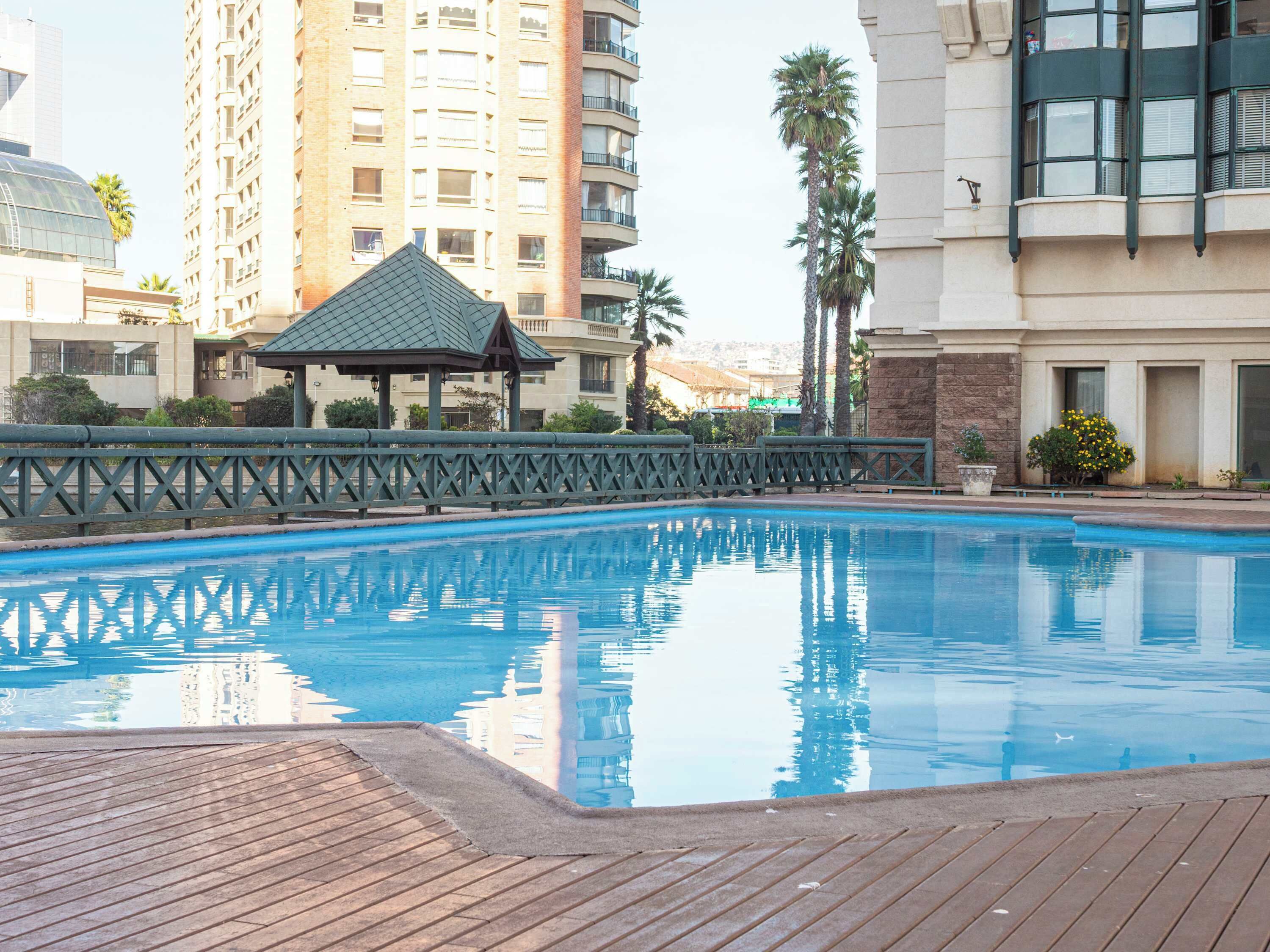 Une piscine dotée d’une terrasse en bois, entourée d’une clôture et de palmiers.