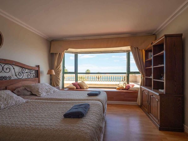 A hotel room with two beds, a large window with a view, a wooden cabinet, and a balcony.