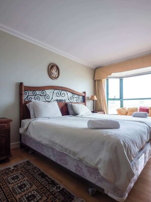 Un dormitorio con cama de madera, cabecera decorativa, ventana con cortinas y una alfombra estampada.