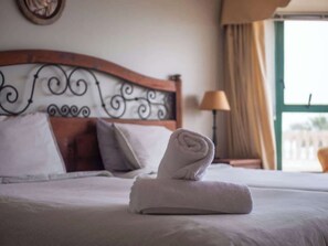 A neatly made bed with a rolled white towel, a wooden headboard with a decorative metal design, and a window with curtains.