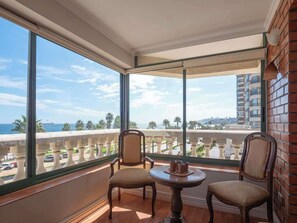 A balcony with two chairs and a table, overlooking a cityscape and a body of water.