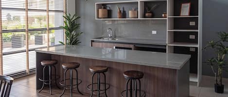 A modern kitchen with a central island, bar stools, pendant lighting, and built-in shelves.