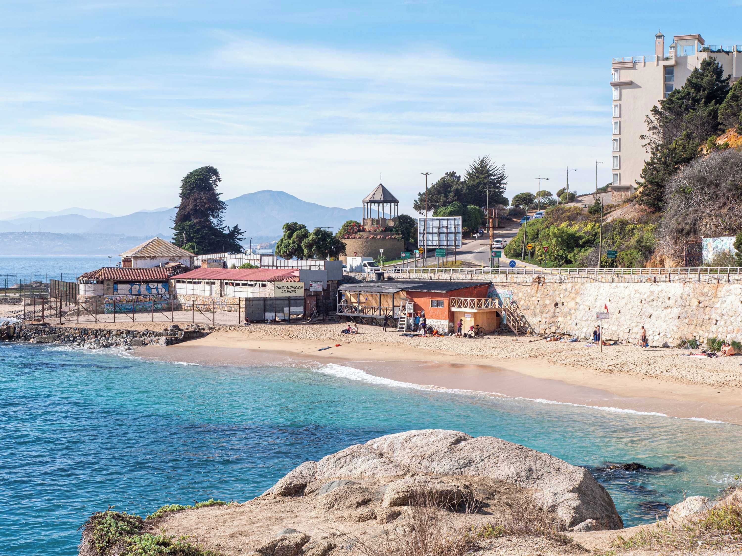 A coastal town with a beach, a small building labeled 'Restaurante Llenes,' and a stone wall.